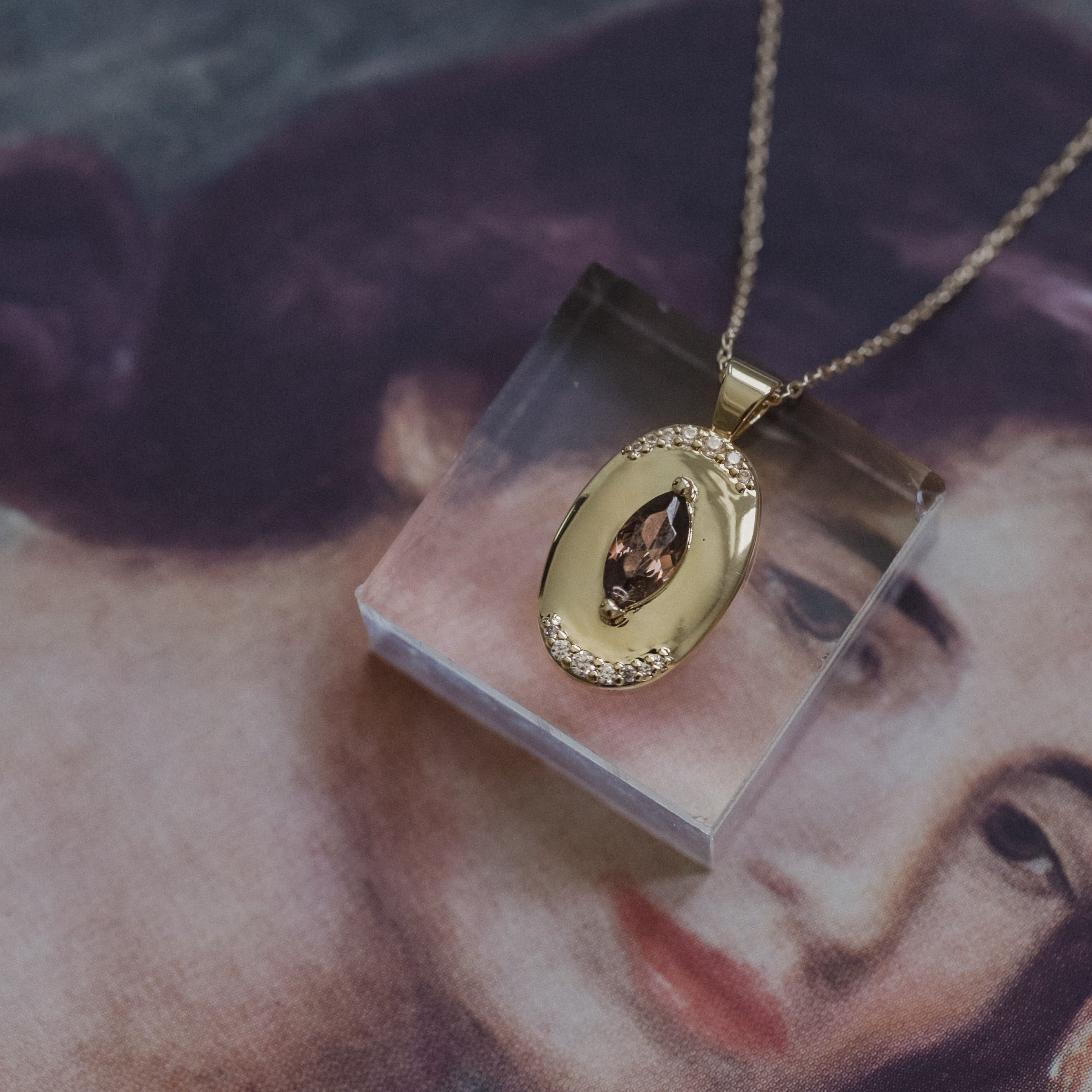 Gold necklace with a pendant on a clear stand against a blurred portrait background